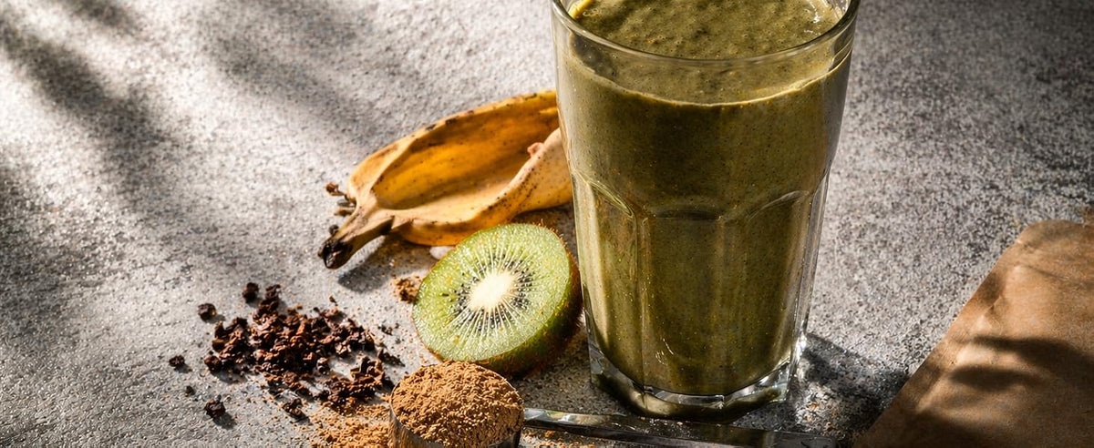 Vaso de smoothie verde con kiwi, plátano y polvo de setas sobre superficie gris